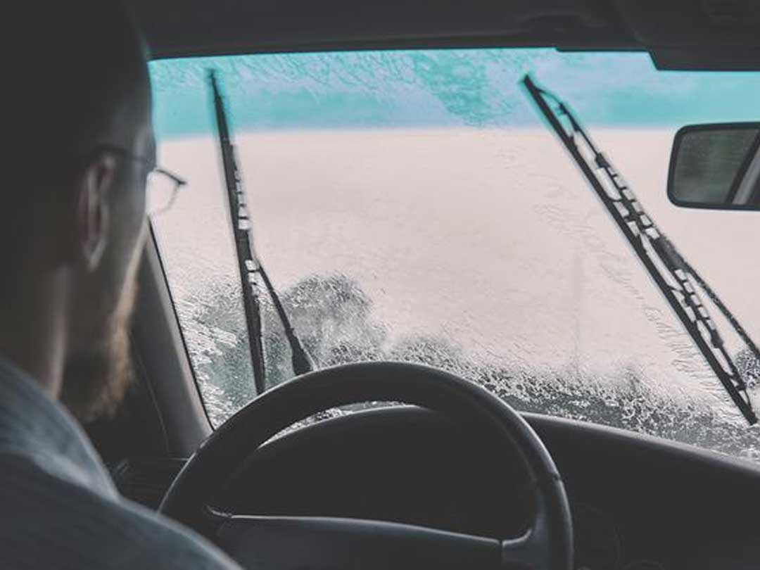 A man driving looking through a car windshield covered in rain
