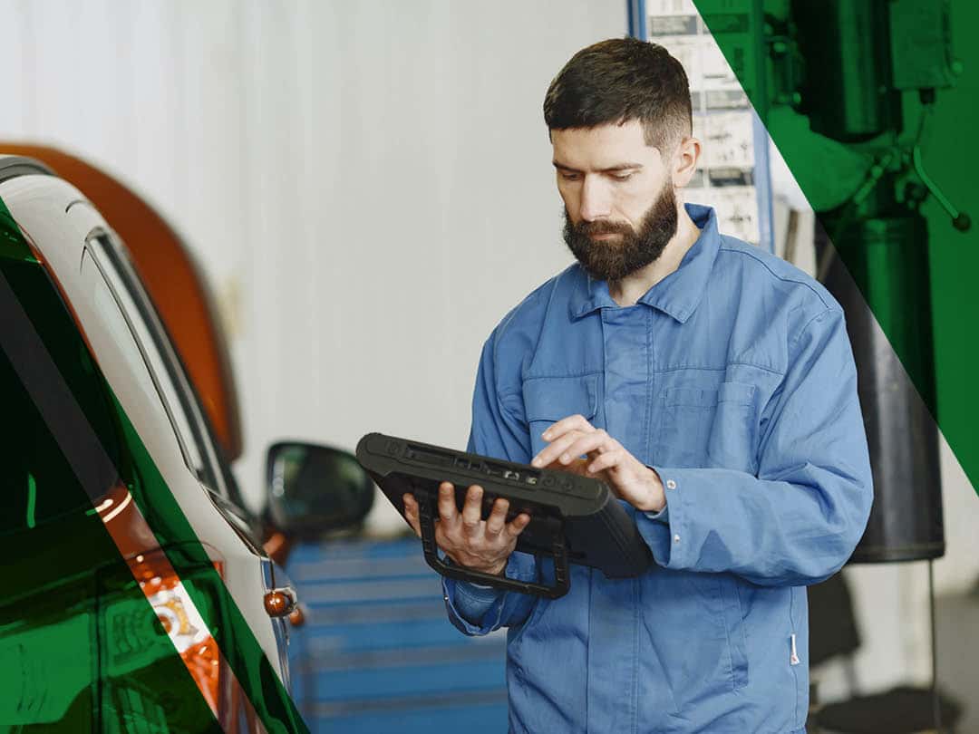 A man in blue coveralls standing beside an orange car carrying out engine diagnostics